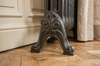 Pied de radiateur en fonte avec motifs décoratifs posé sur un parquet en chêne dans un appartement haussmannien